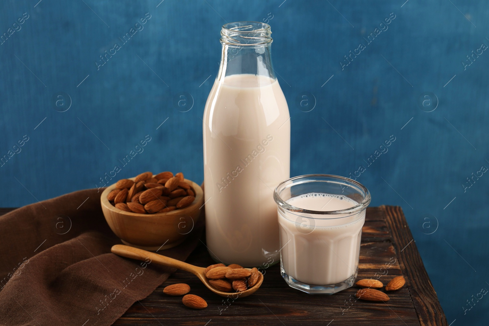 Photo of Fresh almond milk in bottle, glass, nuts and spoon on wooden table