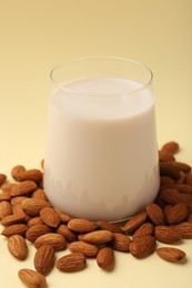 Photo of Fresh almond milk in glass and nuts on beige background