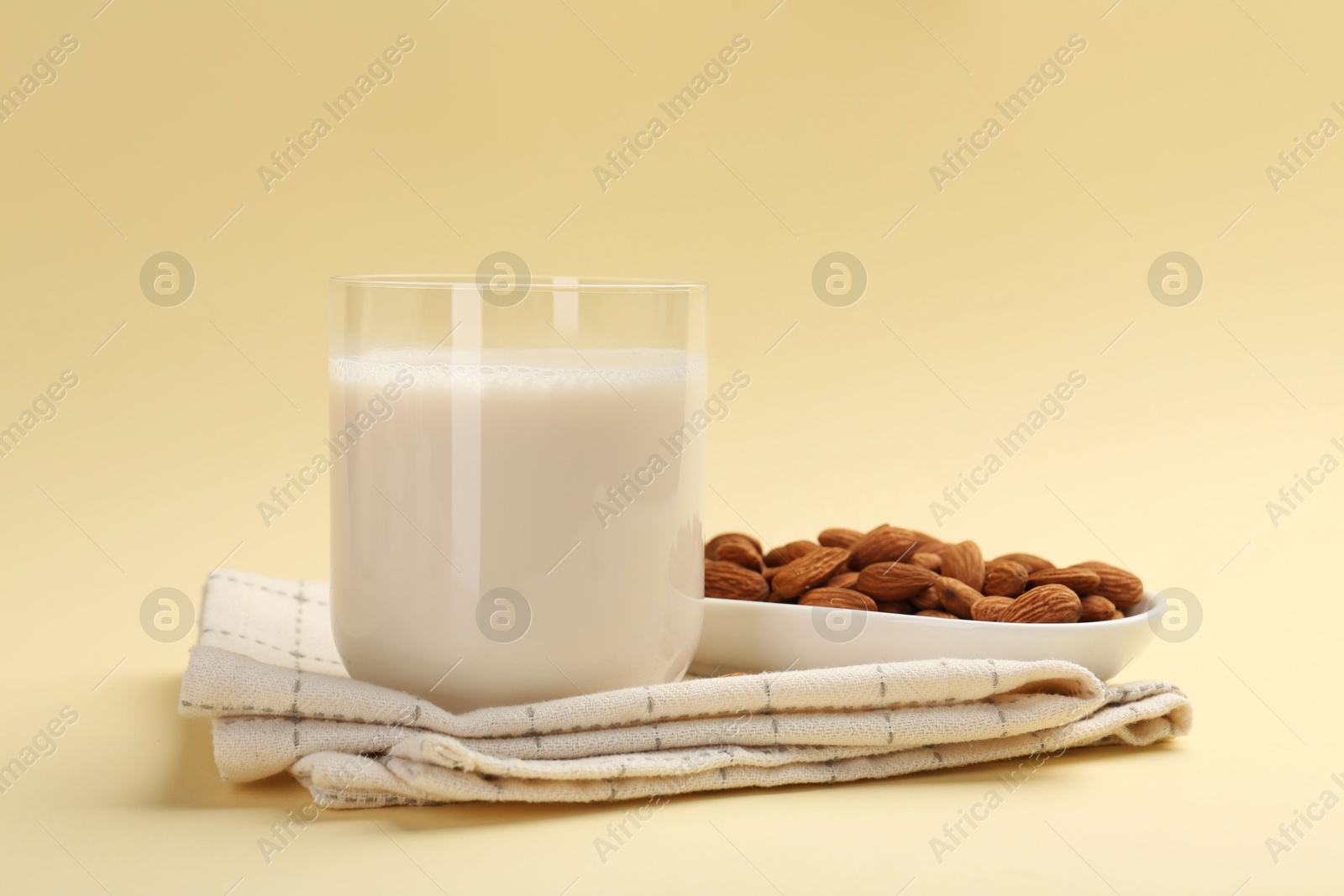 Photo of Fresh almond milk in glass and nuts on beige background