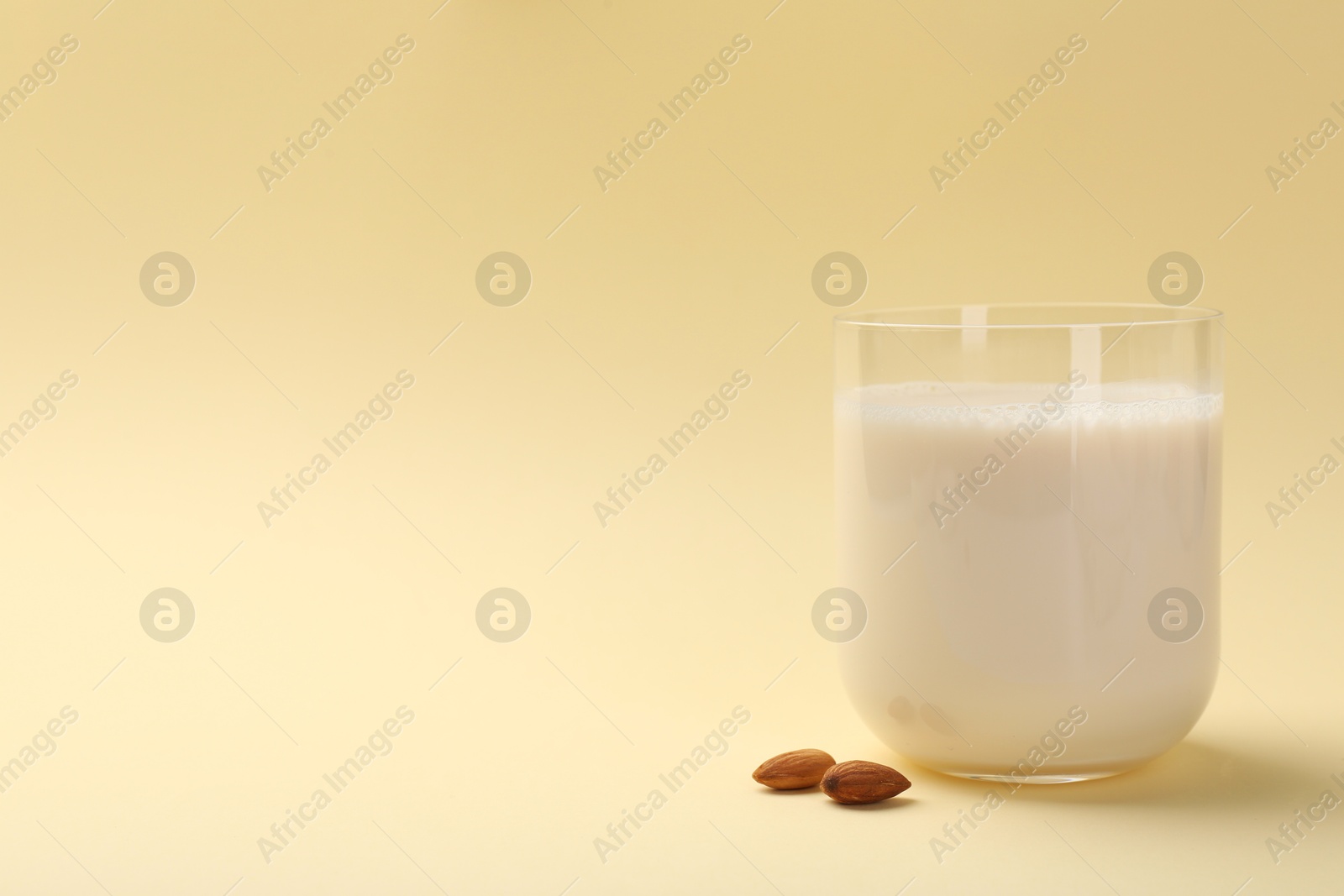 Photo of Fresh almond milk in glass and nuts on beige background, space for text