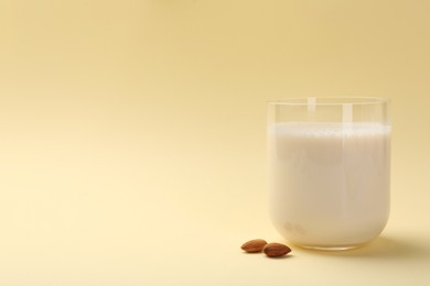 Photo of Fresh almond milk in glass and nuts on beige background, space for text