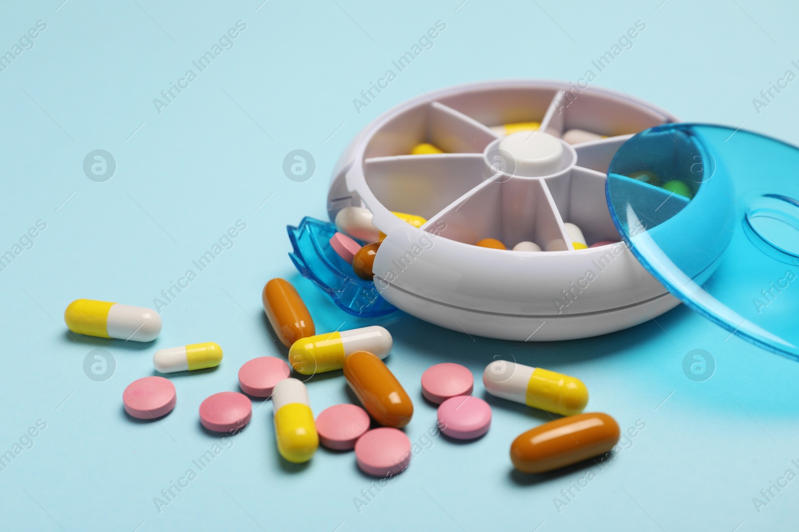 Photo of Different pills and organizer on light blue background, closeup