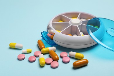 Photo of Different pills and organizer on light blue background, closeup