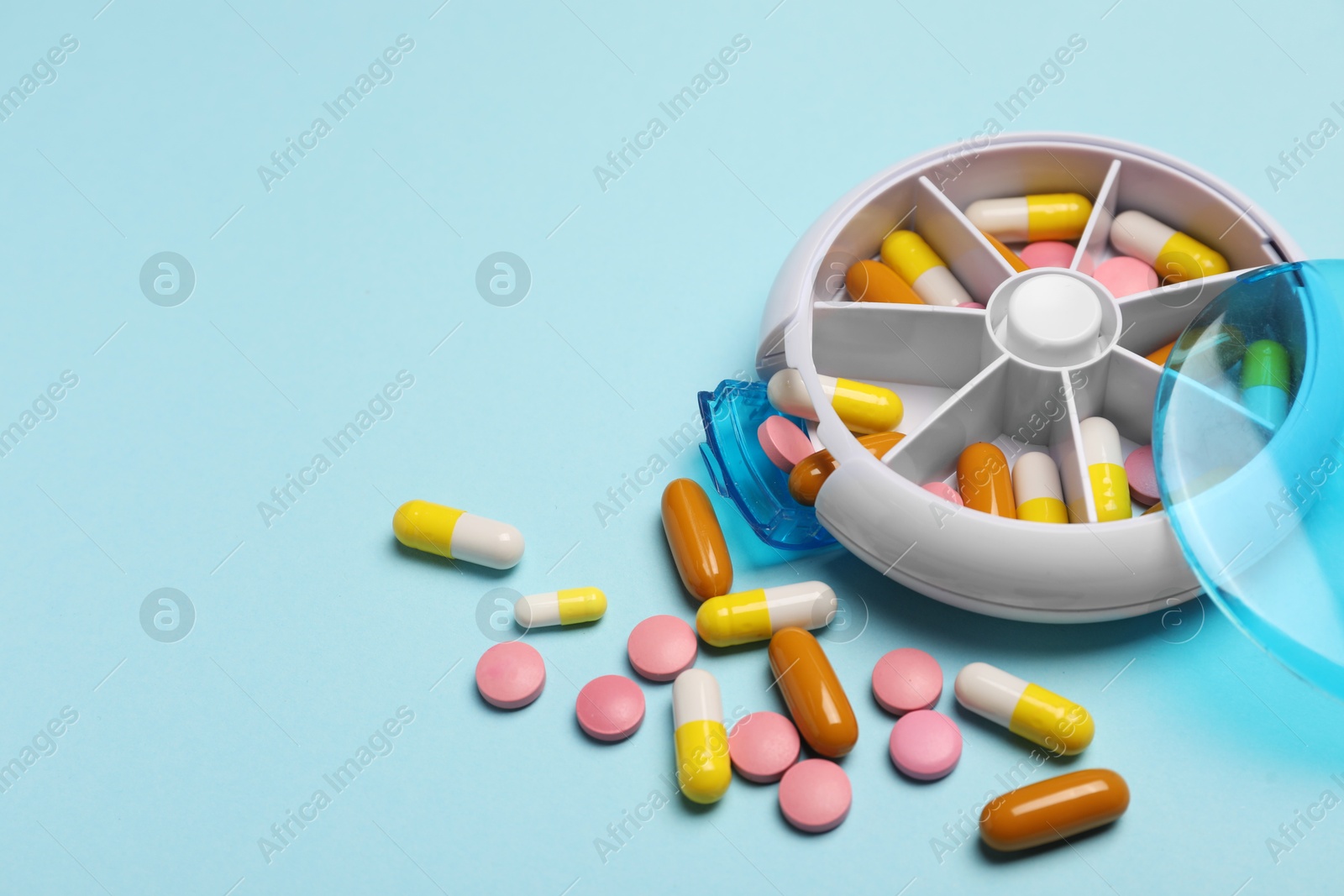 Photo of Different pills and organizer on light blue background, space for text