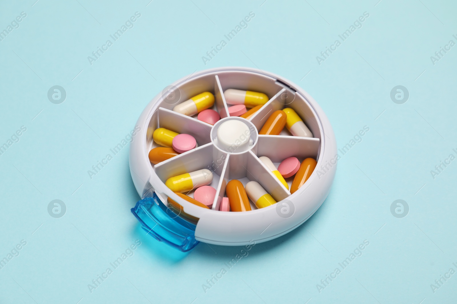 Photo of Different pills in organizer on light blue background