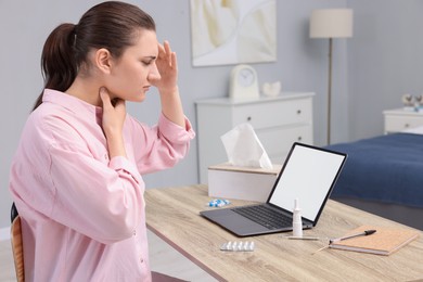 Sick woman having online consultation with doctor via laptop at wooden table indoors