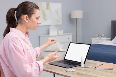 Sick woman having online consultation with doctor via laptop at wooden table indoors