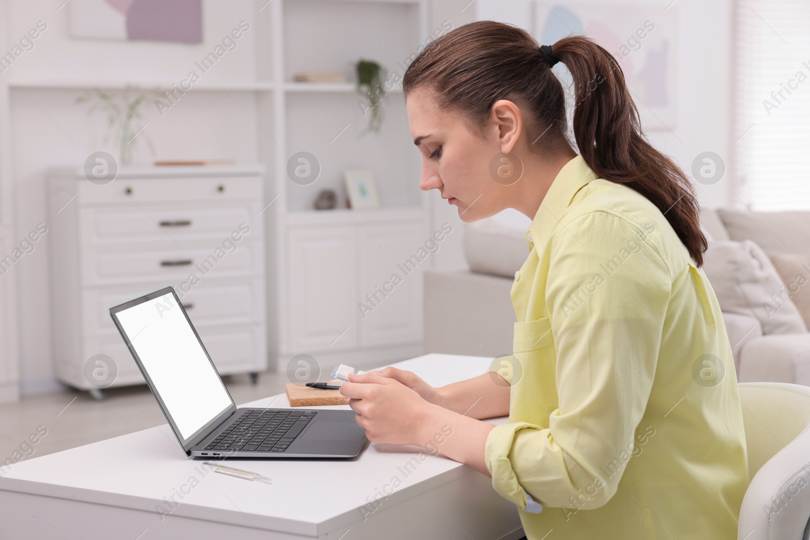 Photo of Sick woman with pills having online consultation with doctor via laptop at white table indoors