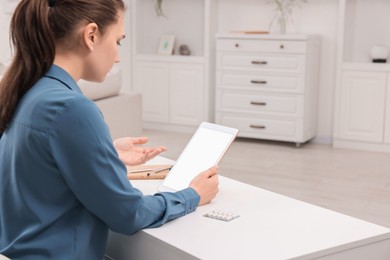 Sick woman having online consultation with doctor via tablet at white table indoors