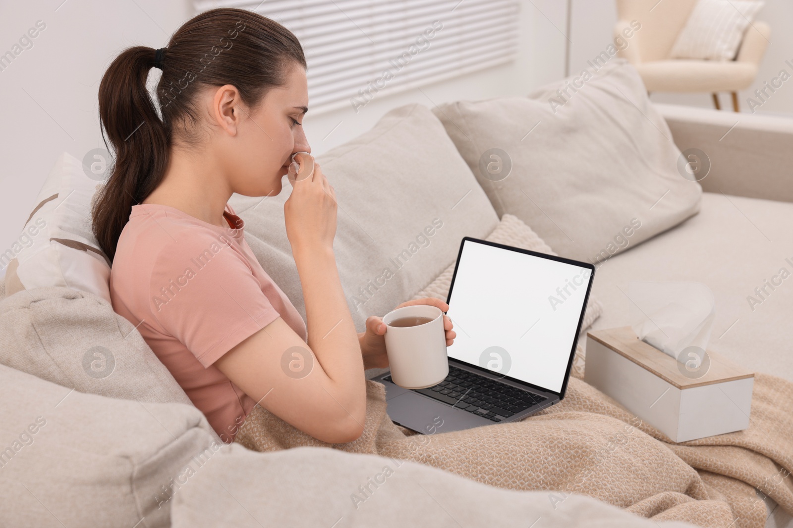 Photo of Sick woman with cup of tea having online consultation with doctor via laptop at home