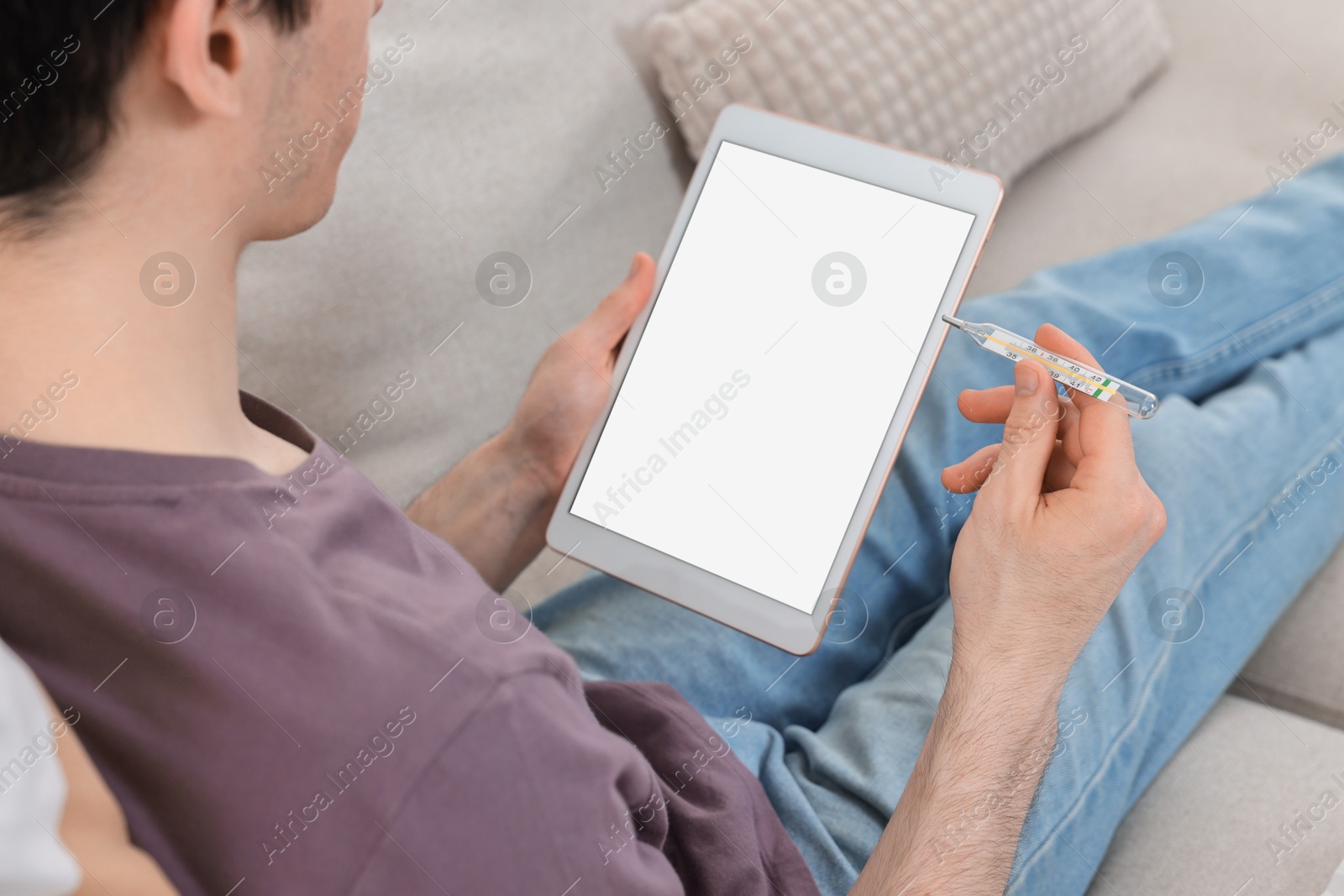 Photo of Sick man with thermometer having online consultation with doctor via tablet at home, closeup