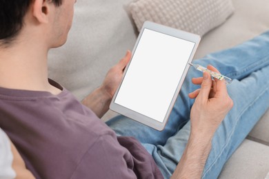 Photo of Sick man with thermometer having online consultation with doctor via tablet at home, closeup