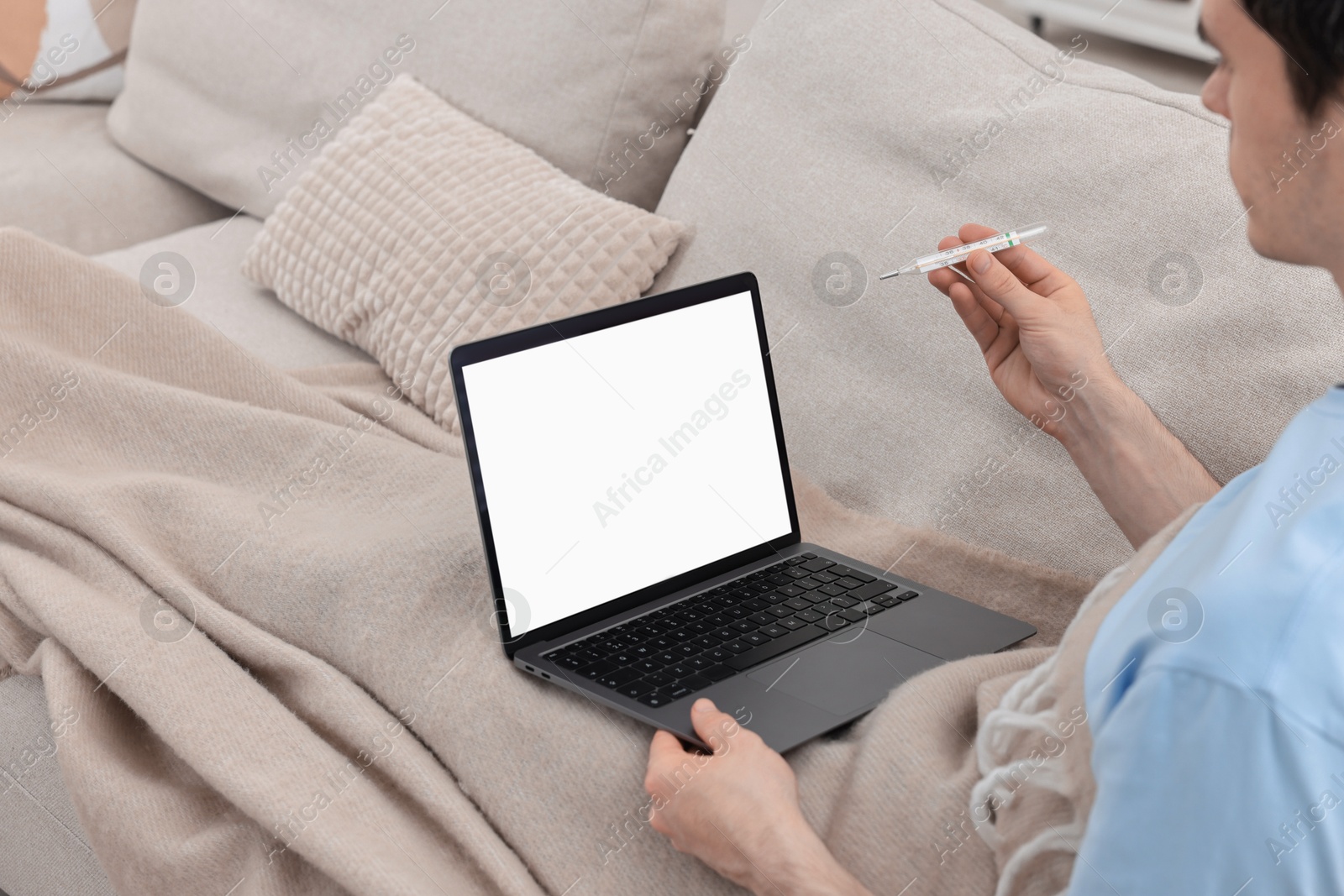 Photo of Sick man with thermometer having online consultation with doctor via laptop at home