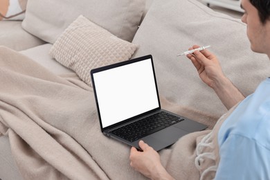 Photo of Sick man with thermometer having online consultation with doctor via laptop at home