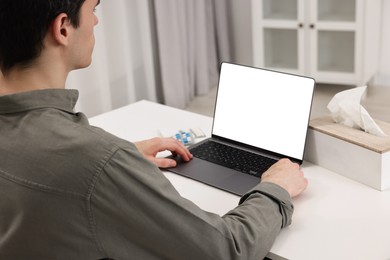 Sick man having online consultation with doctor via laptop at white table indoors