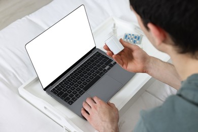 Sick man with pills having online consultation with doctor via laptop at home, closeup