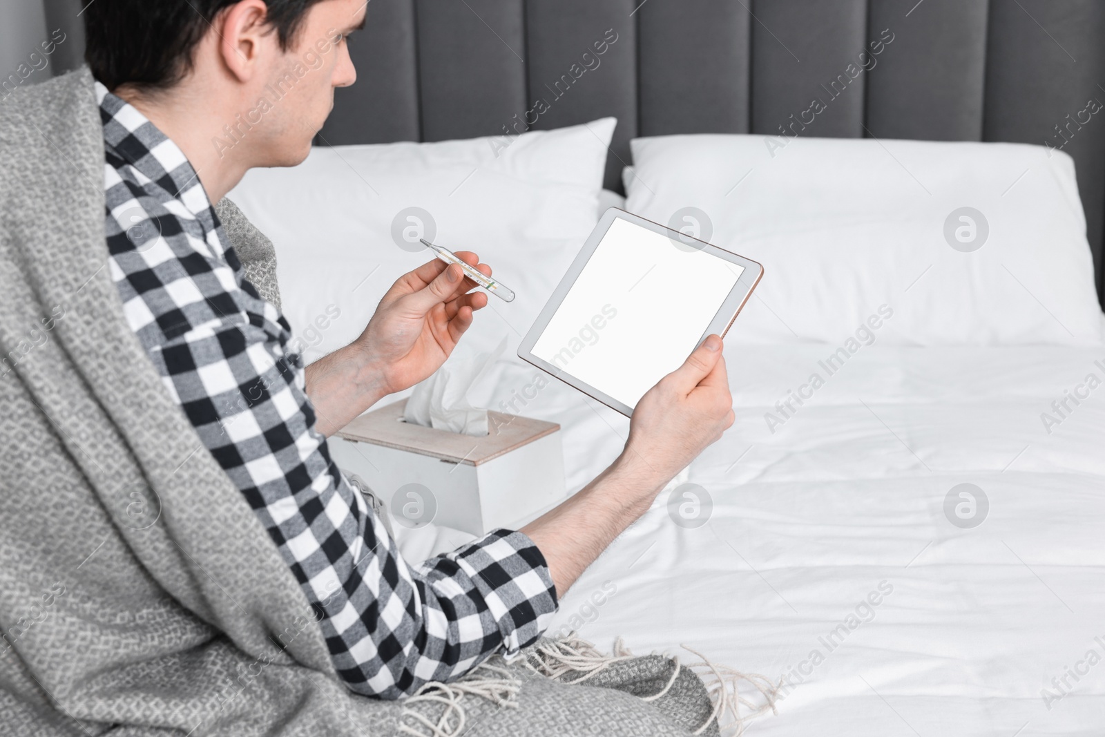 Photo of Sick man with thermometer having online consultation with doctor via tablet at home