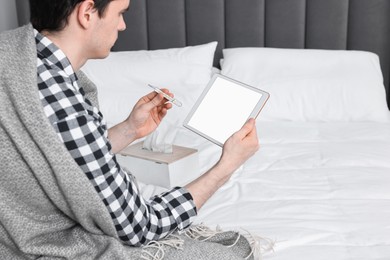 Photo of Sick man with thermometer having online consultation with doctor via tablet at home