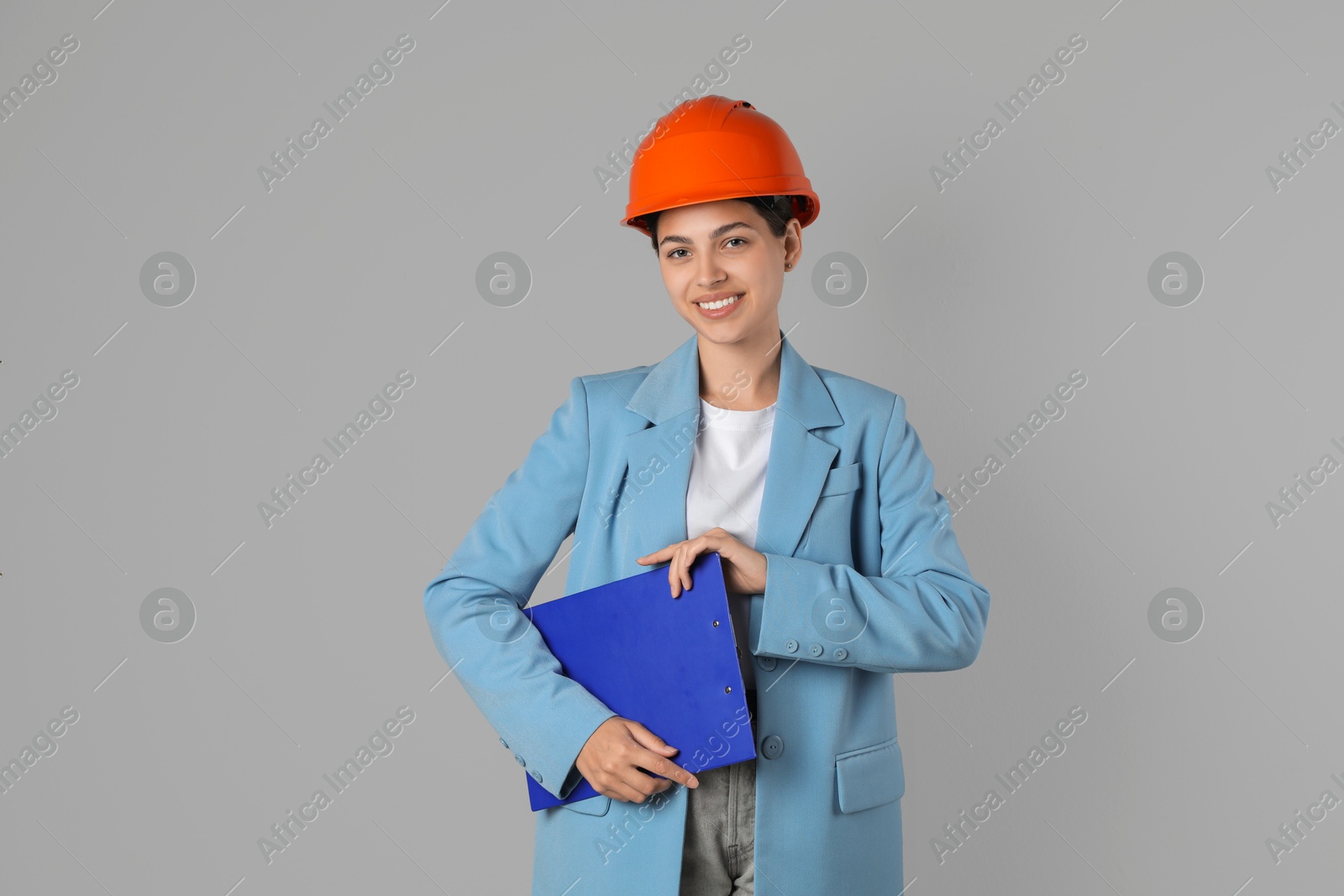 Photo of Engineer in hard hat with clipboard on grey background