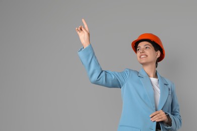 Engineer in hard hat pointing at something on grey background, space for text