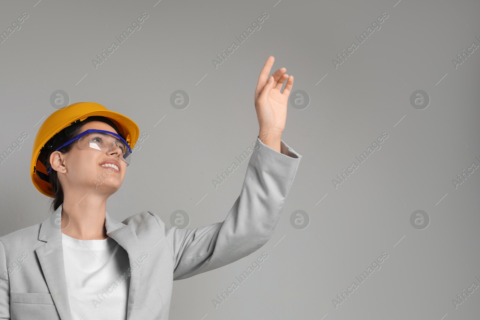 Photo of Engineer in hard hat pointing at something on grey background, space for text