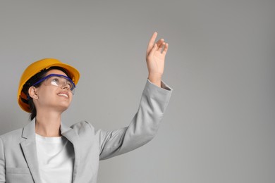 Engineer in hard hat pointing at something on grey background, space for text