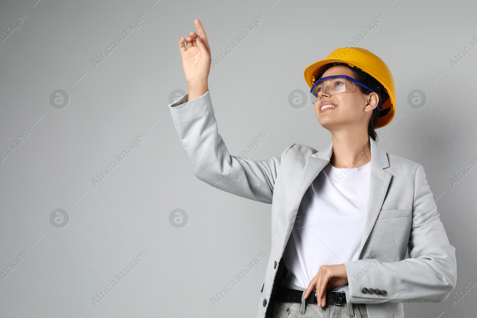 Photo of Engineer in hard hat pointing at something on grey background, space for text