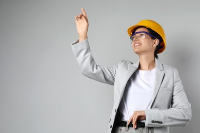 Engineer in hard hat pointing at something on grey background, space for text