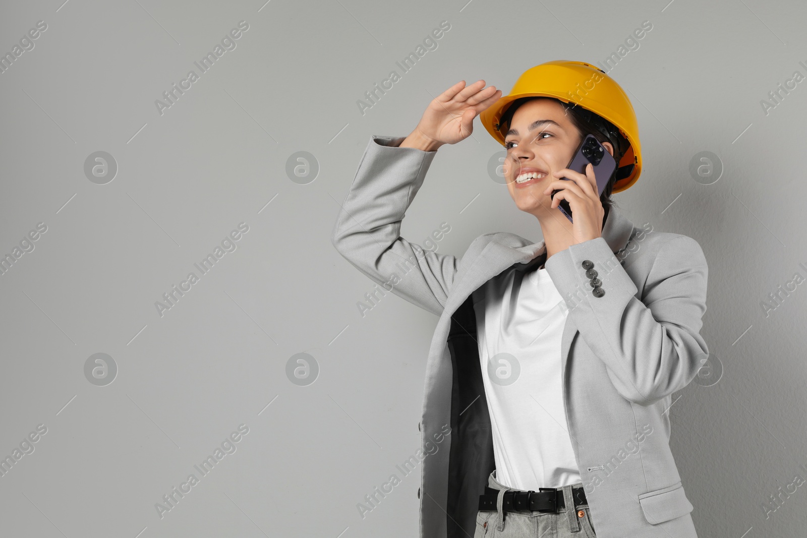 Photo of Engineer in hard hat talking on smartphone against grey background, space for text