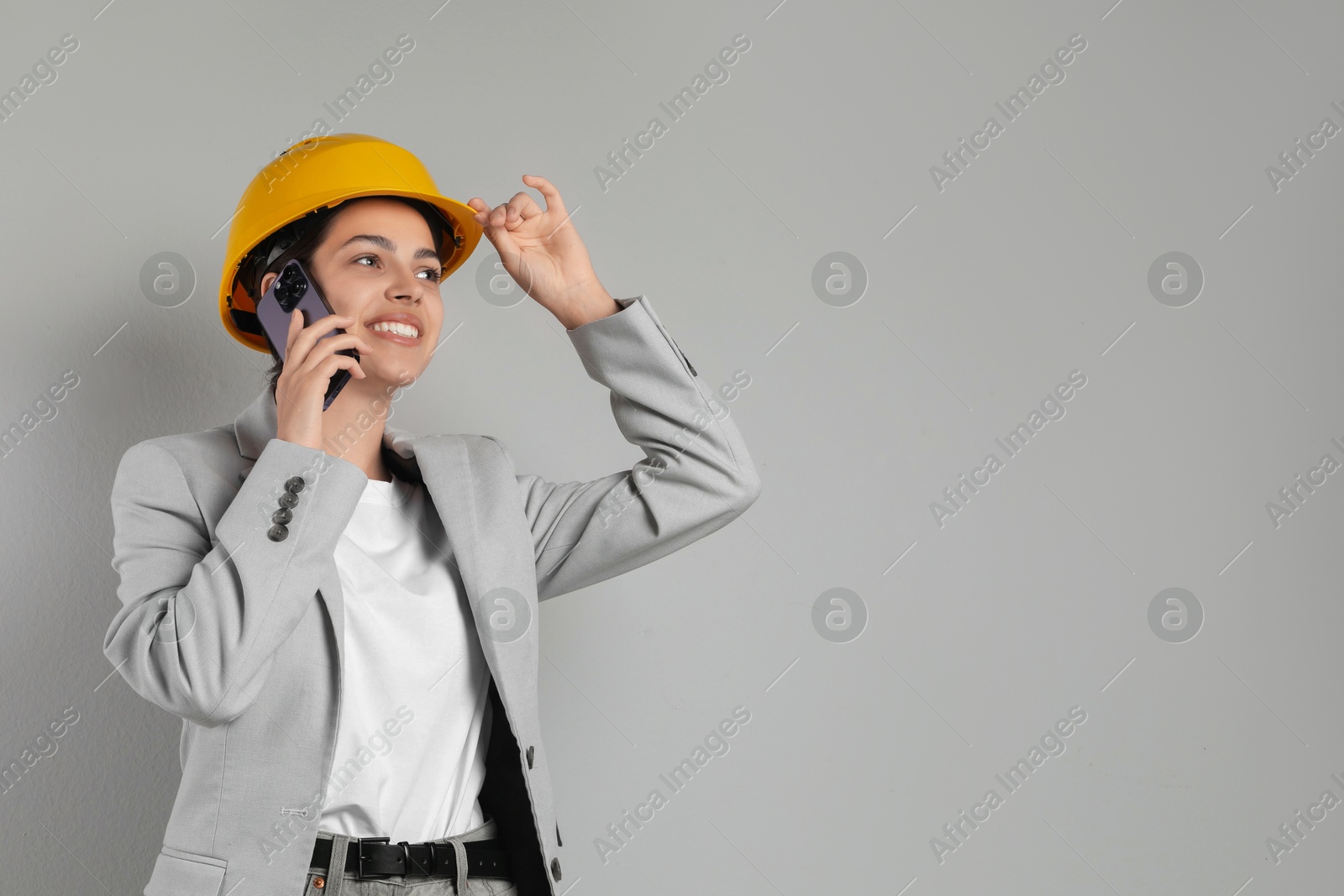 Photo of Engineer in hard hat talking on smartphone against grey background, space for text