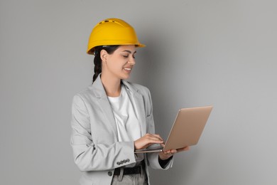 Engineer in hard hat with laptop on grey background