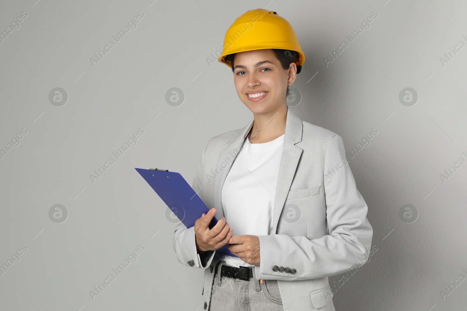 Photo of Engineer in hard hat with clipboard on grey background