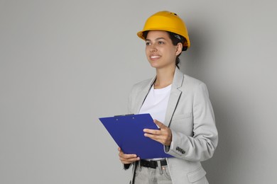 Engineer in hard hat with clipboard on grey background, space for text