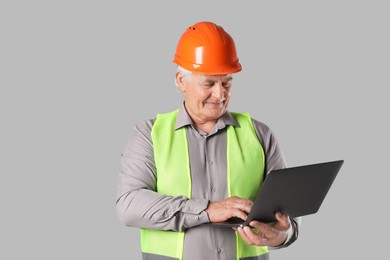 Engineer in hard hat with laptop on grey background, space for text