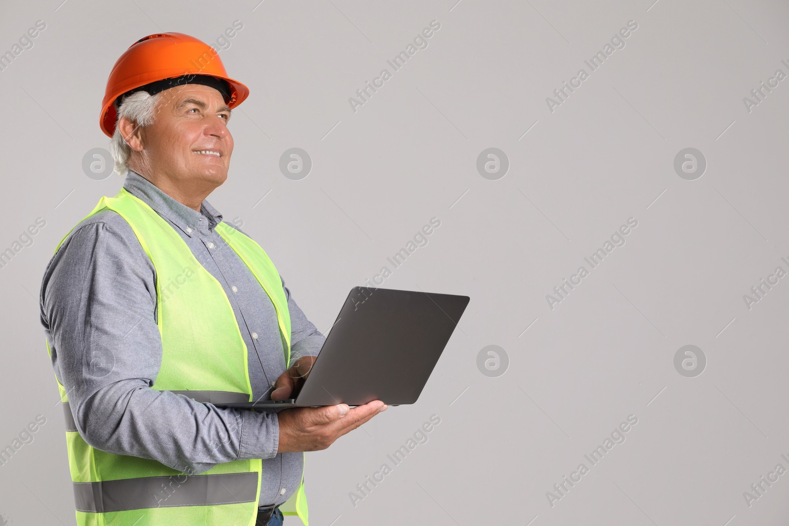 Photo of Engineer in hard hat with laptop on grey background, space for text