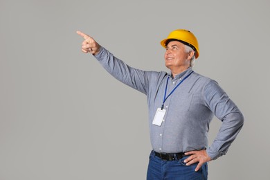 Engineer in hard hat pointing at something on grey background, space for text