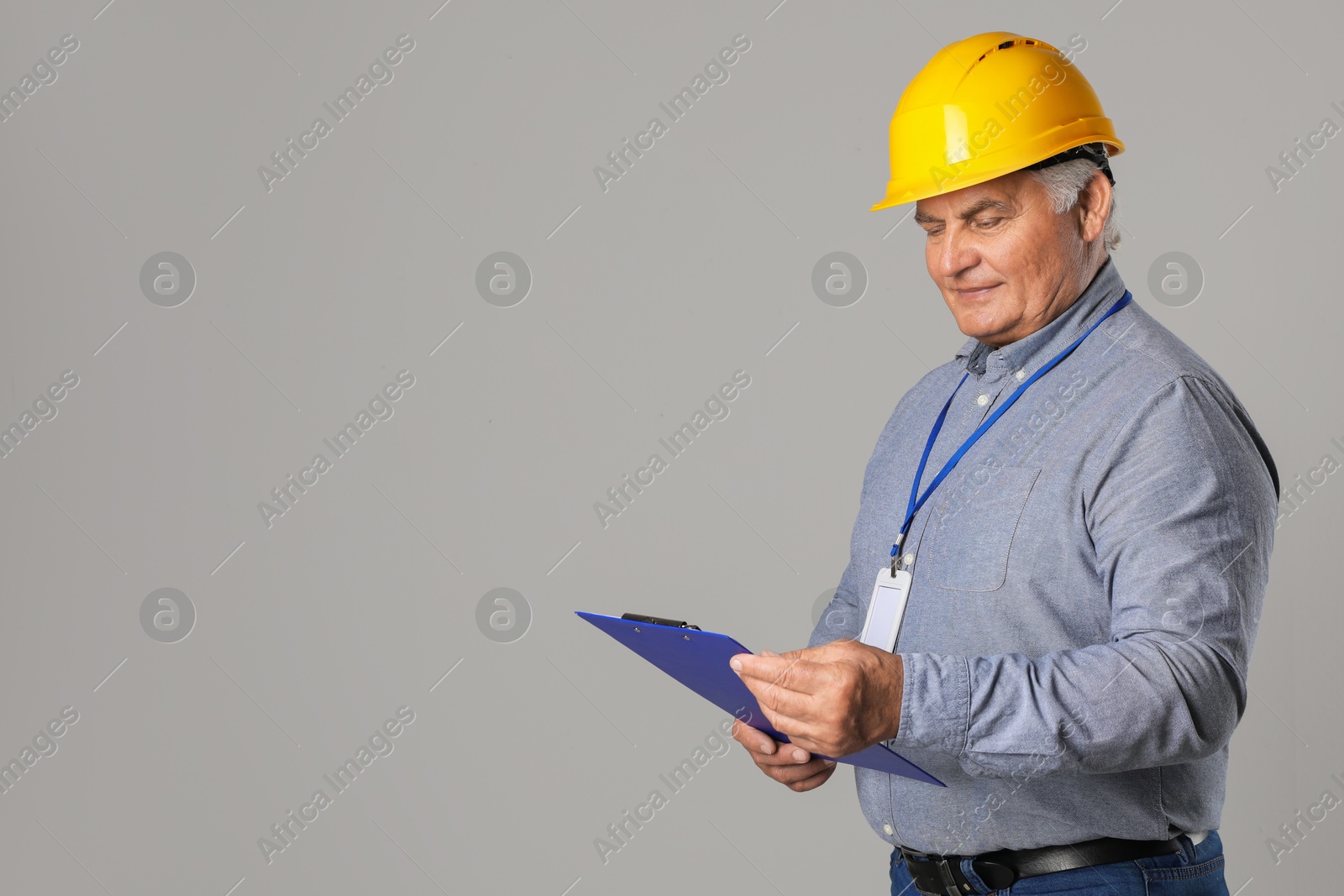 Photo of Engineer in hard hat with clipboard on grey background, space for text