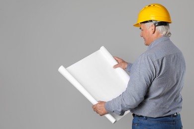 Photo of Engineer in hard hat with draft on grey background, space for text