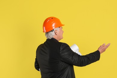 Engineer in hard hat with drafts on yellow background, space for text