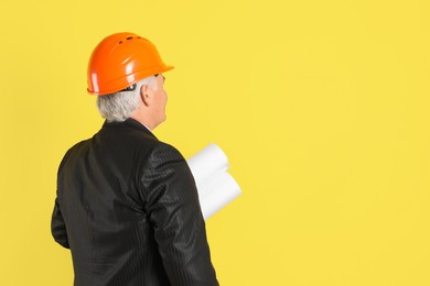 Photo of Engineer in hard hat with drafts on yellow background, space for text