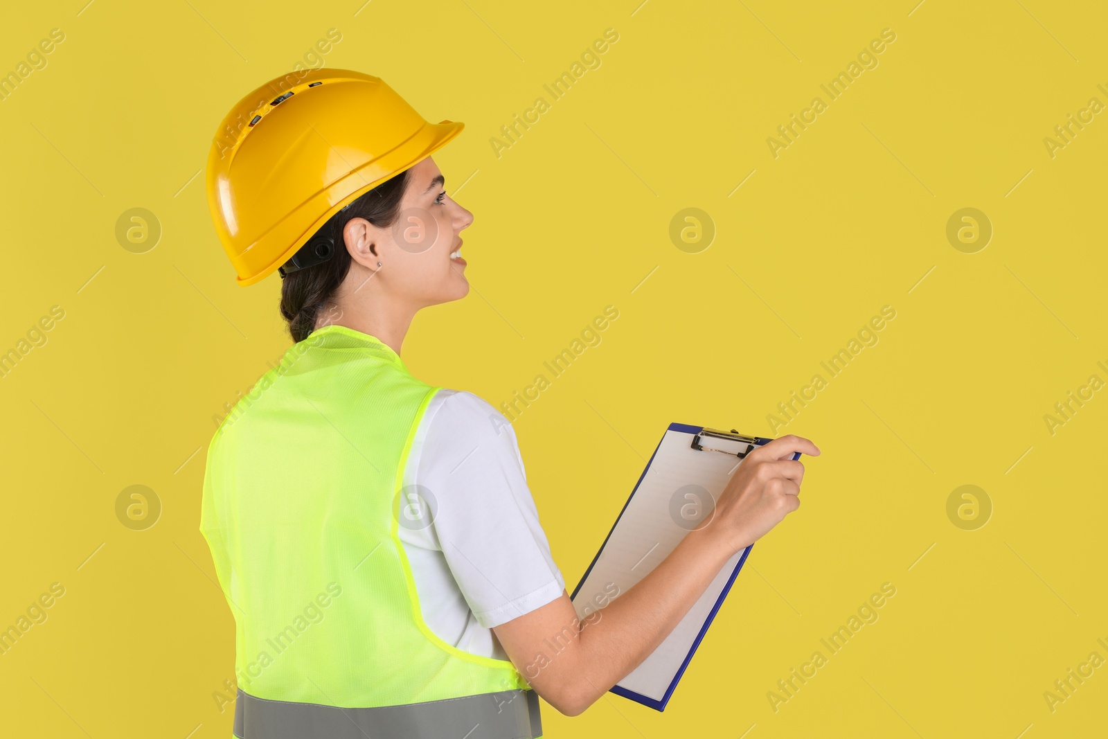 Photo of Engineer in hard hat with clipboard on yellow background