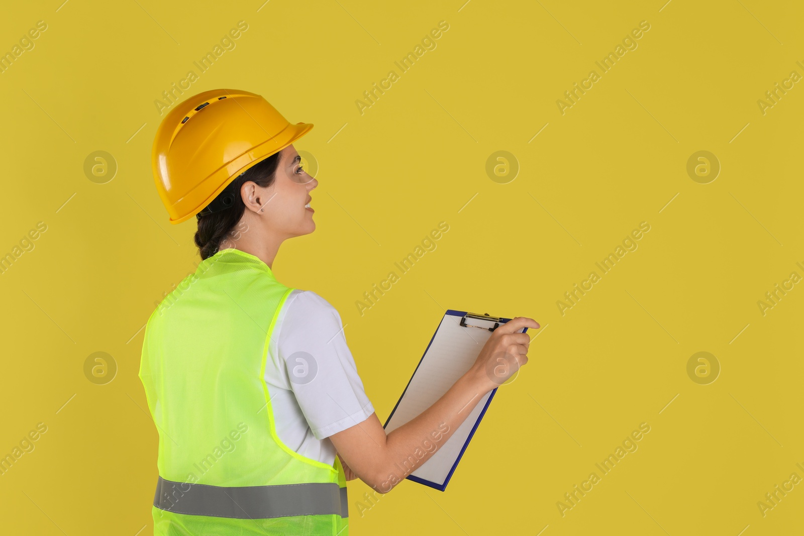 Photo of Engineer in hard hat with clipboard on yellow background, space for text