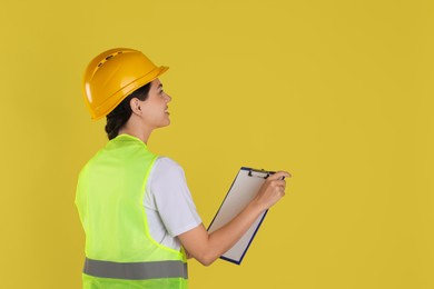 Engineer in hard hat with clipboard on yellow background, space for text