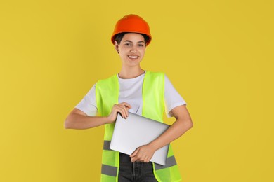 Engineer in hard hat with laptop on yellow background