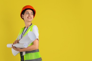 Photo of Engineer in hard hat with drafts on yellow background, space for text