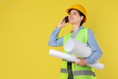 Photo of Engineer in hard hat with drafts talking on smartphone against yellow background, space for text