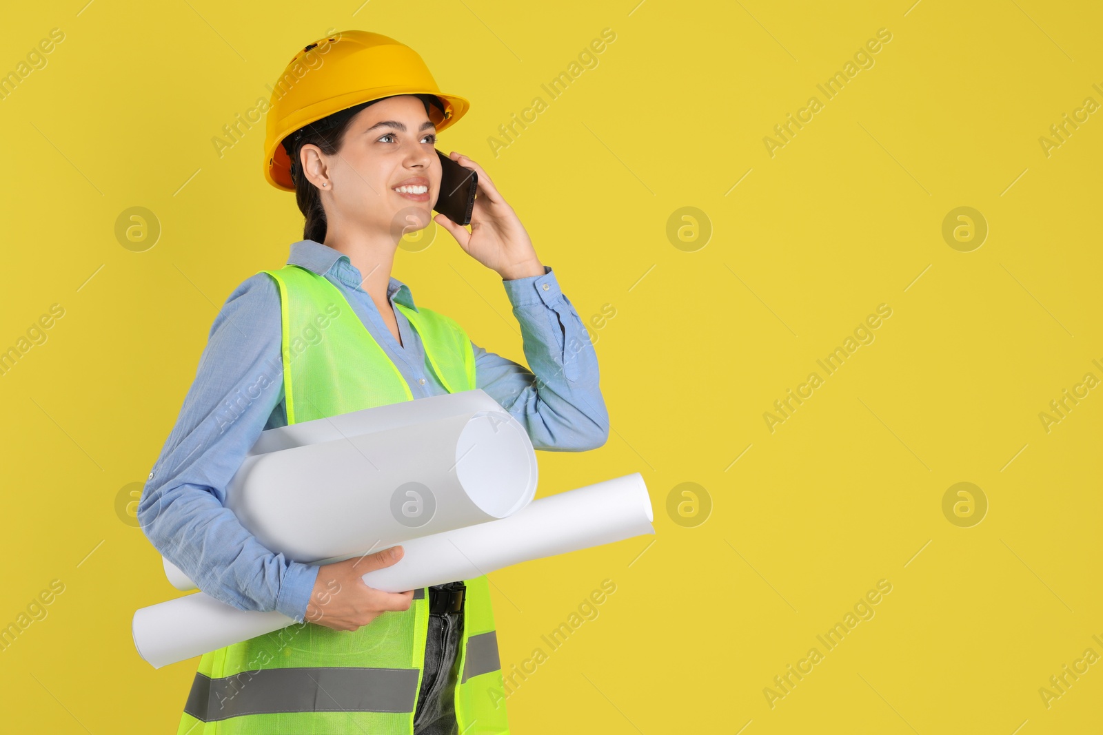 Photo of Engineer in hard hat with drafts talking on smartphone against yellow background, space for text