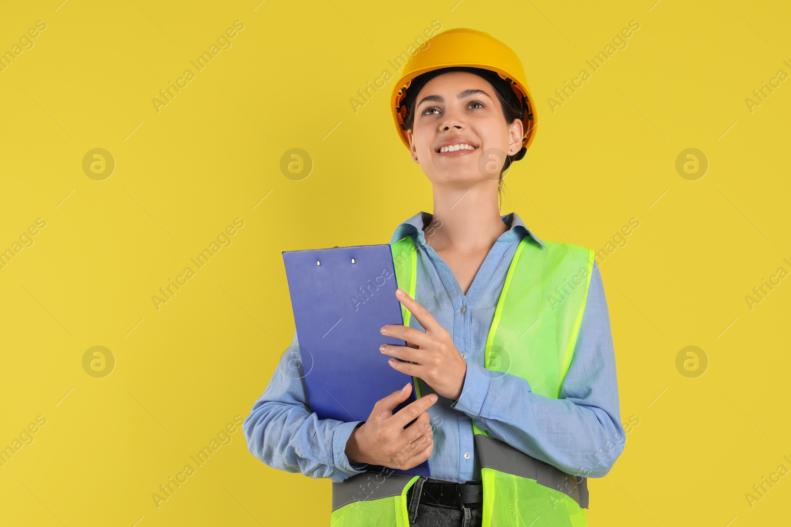 Photo of Engineer in hard hat with clipboard on yellow background, space for text