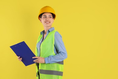 Photo of Engineer in hard hat with clipboard on yellow background, space for text