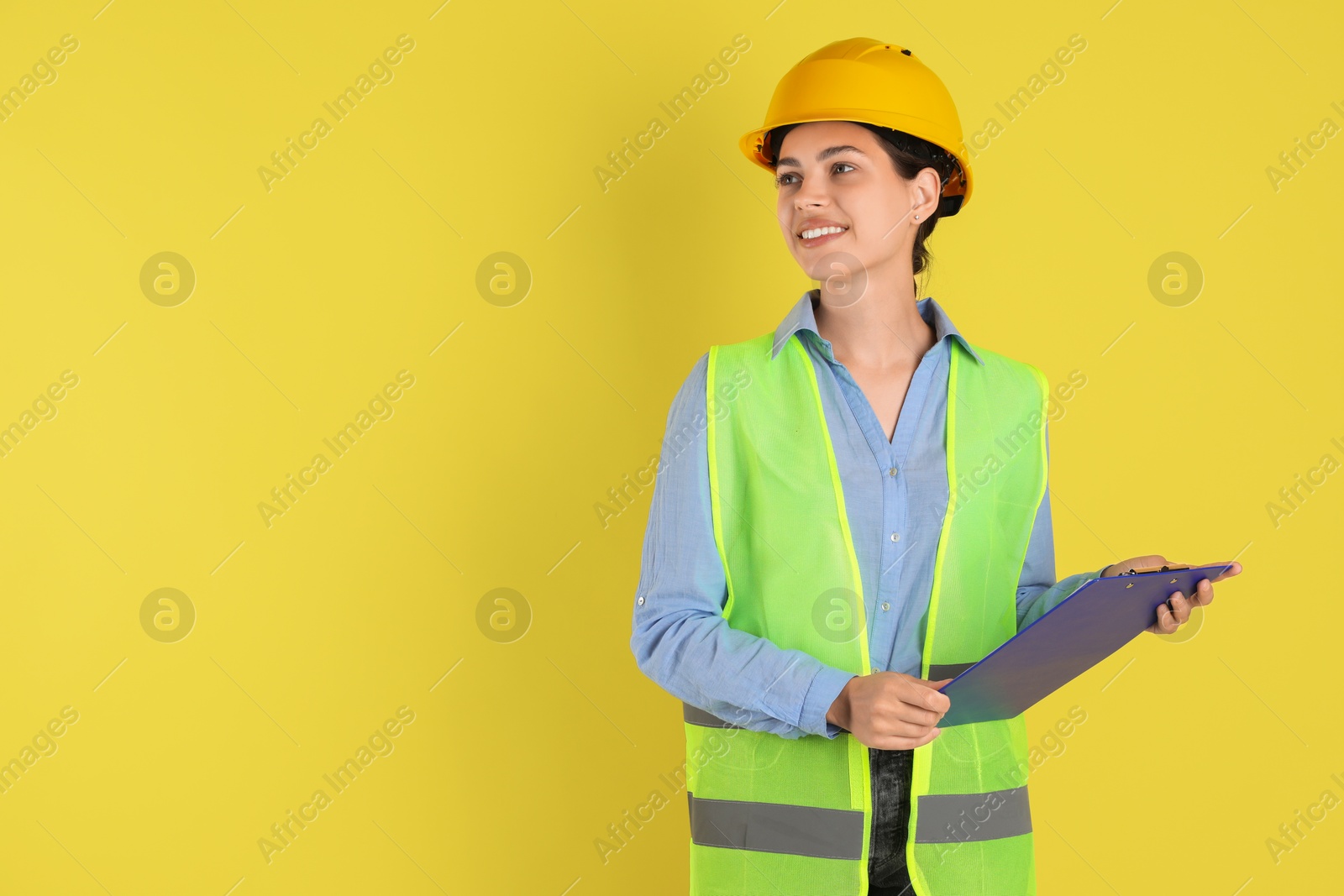 Photo of Engineer in hard hat with clipboard on yellow background, space for text